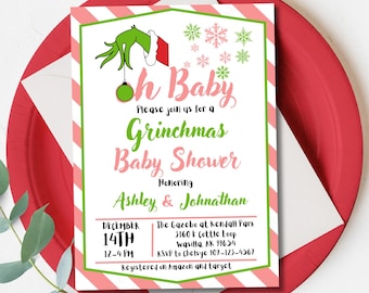 May include: A Grinchmas baby shower invitation with a green and pink color scheme. The invitation features the Grinch's hand holding an ornament, snowflakes, and the text "Oh Baby" and "Grinchmas Baby Shower". The invitation is on a red and white striped plate.