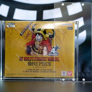 May include: A One Piece Card Game booster box titled The World's Strongest Warriors, featuring a character illustration, enclosed in a clear acrylic magnetic display case. The box displays English Ver. OP-17, 6+, and Bandai Namco branding.