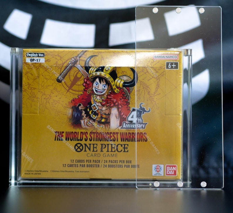 May include: A One Piece Card Game booster box titled The World's Strongest Warriors, featuring a character illustration, enclosed in a clear acrylic magnetic display case. The box displays English Ver. OP-17, 6+, and Bandai Namco branding.