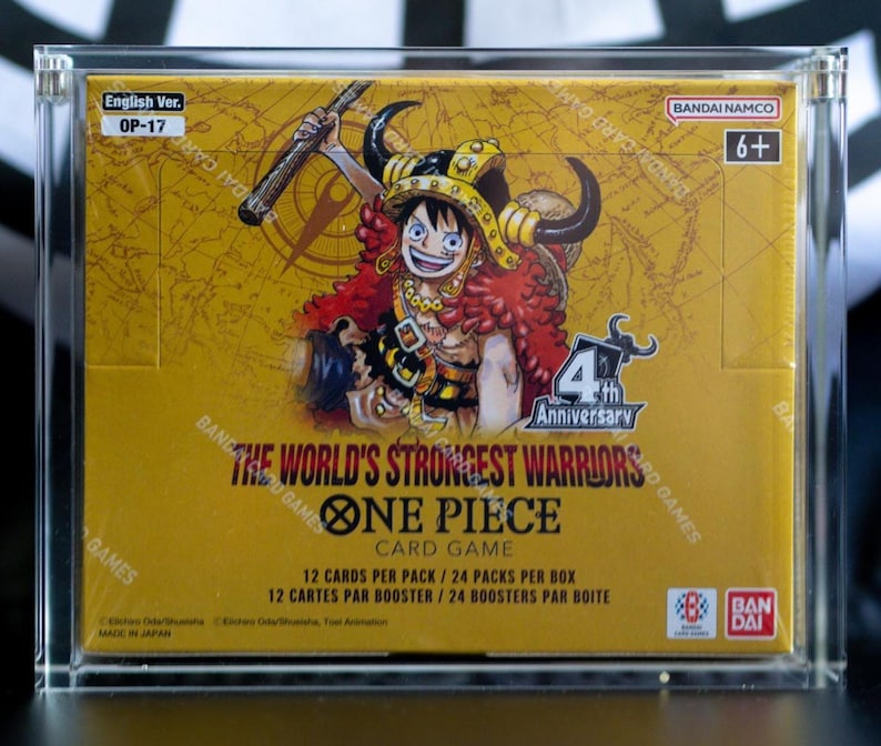 May include: A sealed One Piece Card Game booster box, The World's Strongest Warriors, encased in a clear acrylic display. The yellow box features a character with horns, the 4th Anniversary logo, and text indicating 12 cards per pack, 24 packs per box.