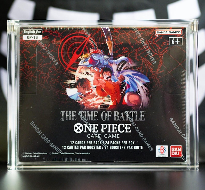 May include: A sealed One Piece Card Game booster box titled The Time of Battle, encased in a clear acrylic display case. The box features colorful anime character illustrations, the Bandai Namco logo, and text indicating 12 cards per pack and 24 packs per box.