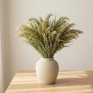 Natural dried canary grass arranged in a neutral ceramic vase on a wooden table with soft daylight