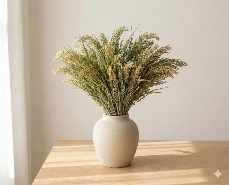 Natural dried canary grass arranged in a neutral ceramic vase on a wooden table with soft daylight
