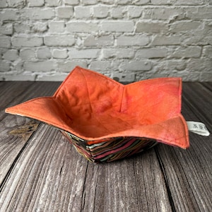 May include: A coral-colored fabric bowl with a black and white geometric pattern. The bowl is folded and ready to be used.