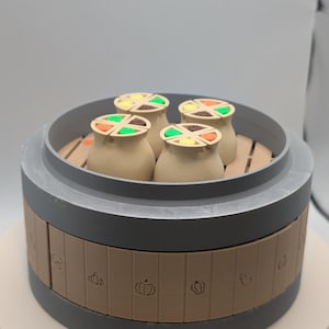 Puede incluir: Una caja de rompecabezas con temática de comida impresa en 3D con cuatro pequeños recipientes de color canela en el interior. Cada recipiente tiene una parte superior segmentada y colorida. La caja es gris y marrón, con iconos relacionados con la comida en el lateral.