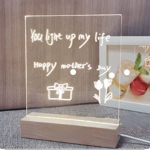 K&ouml;nnte beinhalten: Ein wei&szlig;es, leuchtendes Acrylschild mit dem Text "You light up my life Happy Mother's Day" und einer Zeichnung einer Geschenkbox und zwei Blumen.