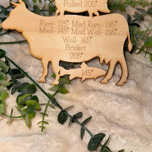 May include: Wooden cutout of a cow, pig, chicken, and fish with internal temperature guidelines for cooking. The cow has the text "Rare - 125° Med Rare - 135° Med - 145° Med Well - 155° Well - 165° Brisket 205°". The pig has the text "145° Pulled 205°". The chicken has the text "165°". The fish has the text "145°".