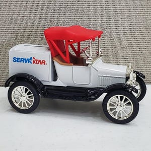 May include: A white toy model of a vintage Ford Model T delivery truck with a red canvas top. The truck has a black chassis and black wheels with silver spokes. The side of the truck has a blue and red logo that reads "SERVISTAR."