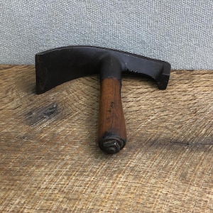May include: A vintage black metal tool with a wooden handle. The tool has a T-shaped design with a flat, rectangular head and a curved, notched edge. The handle is made of dark wood.