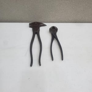 May include: Two vintage black metal pliers. One has a hammer head on the end of the jaws. The other has a curved jaw.
