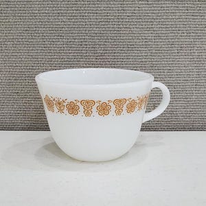 May include: White ceramic teacup with a brown floral pattern around the rim. The cup has a rounded shape and a handle.