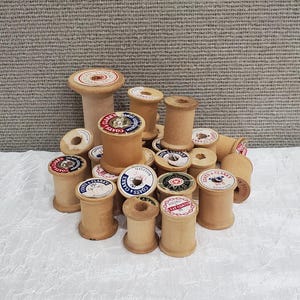 May include: A collection of vintage wooden thread spools with various labels, including "Coats & Clarks" and "J & P Coats". The spools are in various shades of brown and have a worn, antique look.