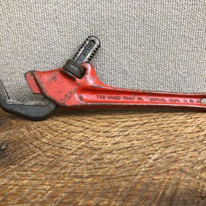 May include: A vintage red and black adjustable wrench. The wrench has a long handle with a loop at the end and a jaw that opens and closes. The text "THE RIDGE TOOL CO. ELYRIA, OHIO, U.S.A." is visible on the handle.