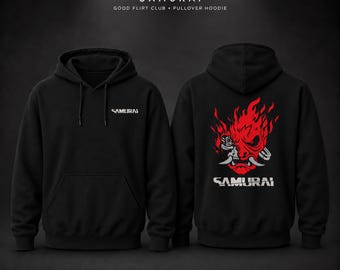 May include: A black pullover hoodie featuring the text SAMURAI on the front left chest. The back displays a large red and white graphic of a stylized robotic face engulfed in flames with the text SAMURAI printed in white below the design.