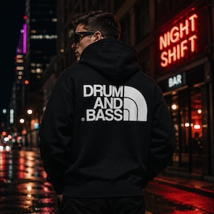 May include: A black hooded sweatshirt featuring a white graphic print on the back that reads DRUM AND BASS in a bold, sans-serif font, accompanied by a stylized curved line design. The hoodie has long sleeves and a hood with a drawstring.