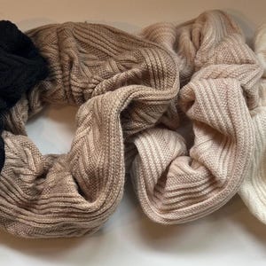 Puede incluir: Cuatro scrunchies en diferentes colores: negro, beige, marrón claro y blanco. Los scrunchies están hechos de un tejido suave y de punto.