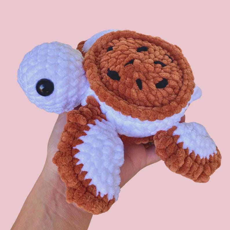 Puede incluir: Un peluche de tortuga hecho a mano con ganchillo en blanco, marr&oacute;n y negro. La tortuga tiene cabeza y extremidades blancas, caparaz&oacute;n marr&oacute;n y ojos negros. El peluche es suave y es ideal como juguete para ni&ntilde;os o decoraci&oacute;n de guarder&iacute;a.