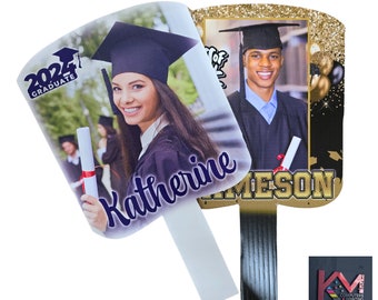 May include: Two graduation fans featuring photos of graduates in caps and gowns. One fan has the text "2024 Graduate" and the name "Katherine". The other fan has the name "Jameson" in gold lettering. Both fans have a white handle.