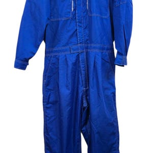 May include: Blue Suzuki mechanic's jumpsuit with the Suzuki logo on the chest. The jumpsuit has multiple pockets, a belt, and white stitching. The workwear is made of a durable material and is designed for mechanics.