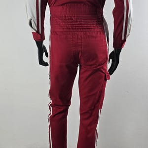 Może przedstawiać: Czerwono-biały kombinezon wyścigowy z napisem "HONDA" na plecach. Kombinezon ma białe paski na rękawach i nogach. Kombinezon jest prezentowany na manekinie.