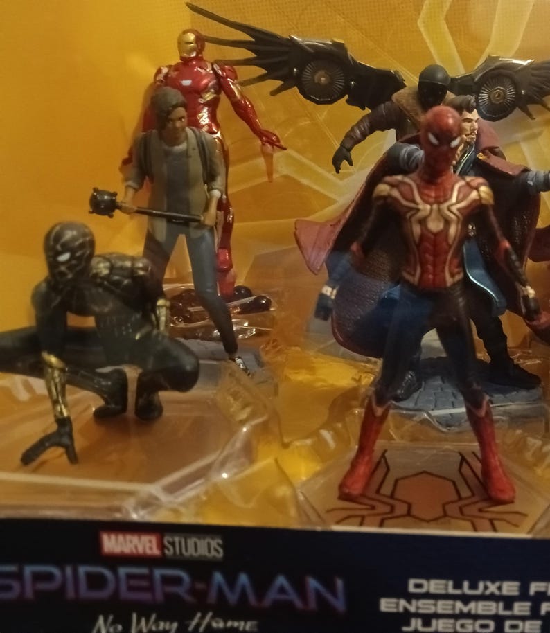 May include: A set of Marvel Studios Spider-Man: No Way Home action figures. The set includes Spider-Man in his red and black suit, Spider-Man in his black suit, Iron Man in his red and gold suit, Doctor Strange in his blue and red robe, and two other figures. The figures are all standing on a brown base with a spider web design.