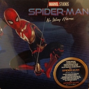 May include: A red and black Spider-Man character with a gold chest plate is shown in a dynamic pose. The background is dark blue with the text "MARVEL STUDIOS" and "SPIDER-MAN No Way Home" in white. The image also features a circular graphic with the text "SPIDER-MAN Home Coming" and "SPIDER-MAN Far From Home".