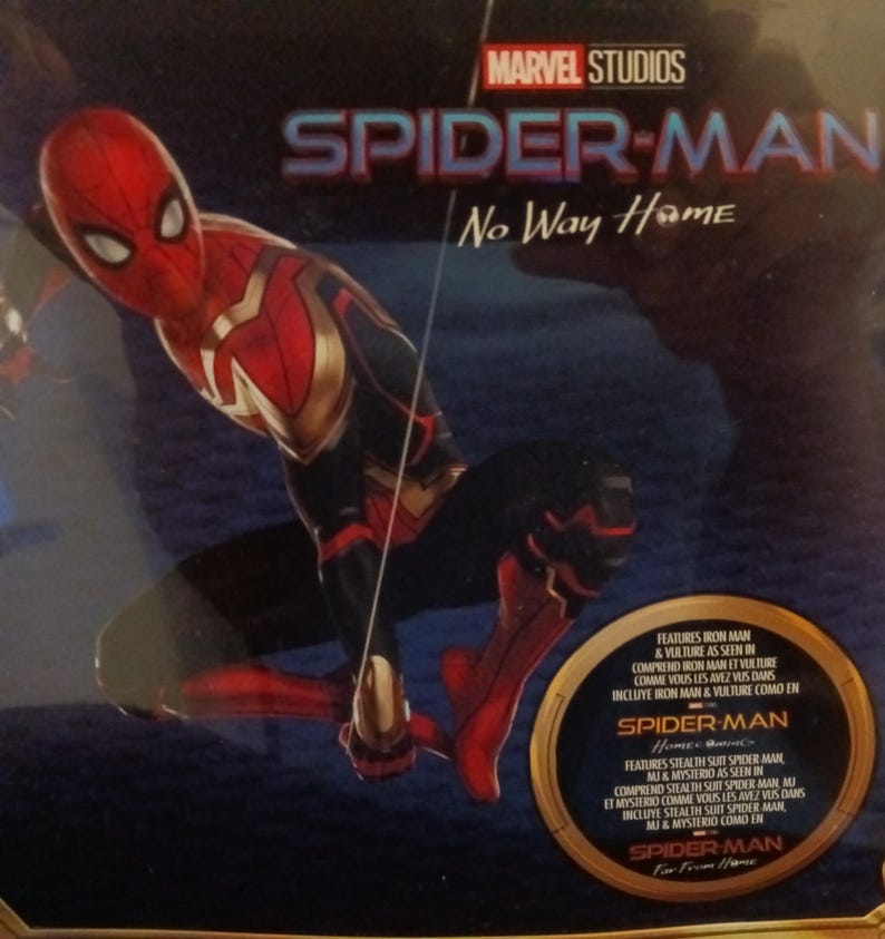May include: A red and black Spider-Man character with a gold chest plate is shown in a dynamic pose. The background is dark blue with the text "MARVEL STUDIOS" and "SPIDER-MAN No Way Home" in white. The image also features a circular graphic with the text "SPIDER-MAN Home Coming" and "SPIDER-MAN Far From Home".
