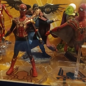 May include: A set of superhero action figures, including Spider-Man, Iron Man, Doctor Strange, and Green Goblin. The figures are posed in dynamic action poses and are made of plastic. The figures are displayed on a black background.