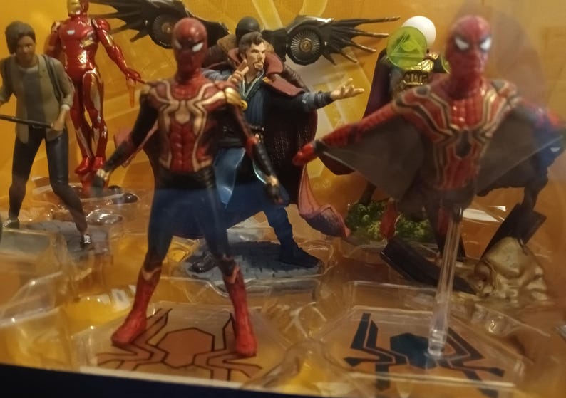May include: A set of superhero action figures, including Spider-Man, Iron Man, Doctor Strange, and Green Goblin. The figures are posed in dynamic action poses and are made of plastic. The figures are displayed on a black background.