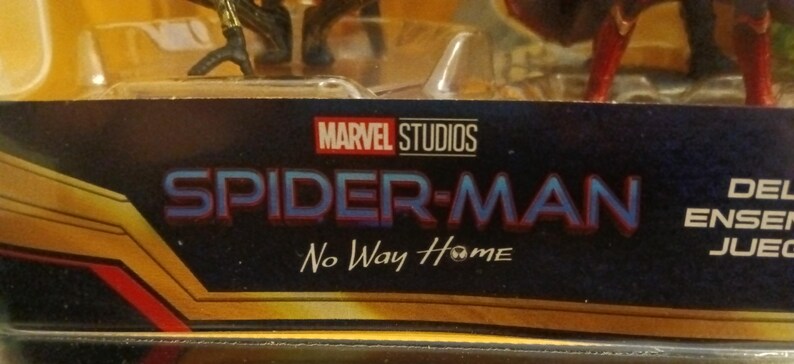 May include: A close-up of a Spider-Man No Way Home toy packaging featuring the Marvel Studios logo and the movie title. The packaging is gold and black with a blue background.