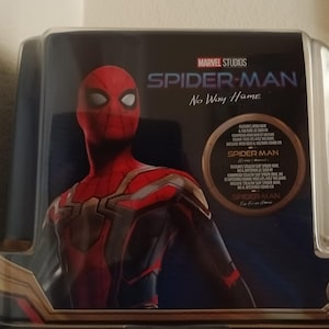 May include: A red and black Spider-Man figure in a clear plastic case with the text "MARVEL STUDIOS SPIDER-MAN No Way Home" on the front. The figure is wearing a red and black suit with a gold spider emblem on the chest.