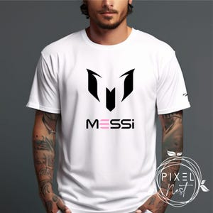 May include: White t-shirt with a black soccer logo and the word "MESSI" in pink letters.
