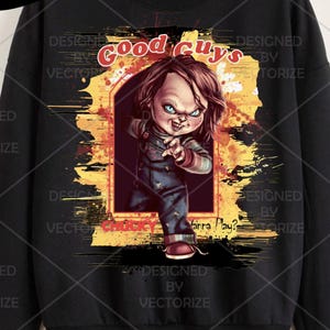 Peut inclure: Un sweat-shirt noir avec une impression graphique représentant une poupée aux cheveux brun-roux et aux yeux bleus portant une salopette bleue. Le texte Good Guys est imprimé au-dessus et CHUCKY Wanna Play? en rouge en dessous.