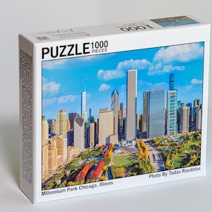 Puede incluir: Un rompecabezas de 1000 piezas que presenta una vista panorámica de Millennium Park en Chicago, Illinois. El rompecabezas muestra el horizonte de la ciudad con rascacielos y un parque con árboles y un escenario. El texto "Photo By Tadas Raudzis" está en la esquina inferior derecha.