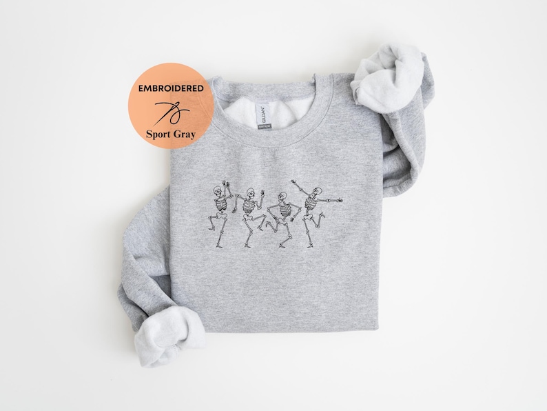 May include: A gray sweatshirt with an embroidered design of four skeletons dancing. The sweatshirt is folded and the tag says "Embroidered Sport Gray".