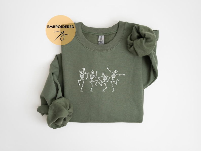 May include: A green sweatshirt with an embroidered design of four skeletons dancing. The sweatshirt has a crew neck and long sleeves.