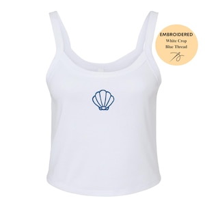 May include: White crop top with a scoop neck and thin straps. The top features a blue embroidered seashell design on the front. A circular graphic in the upper right corner reads "EMBROIDERED White Crop Blue Thread".