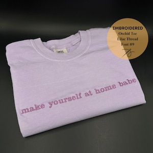 May include: A lavender colored t-shirt with the text "make yourself at home babe" embroidered in pink thread.
