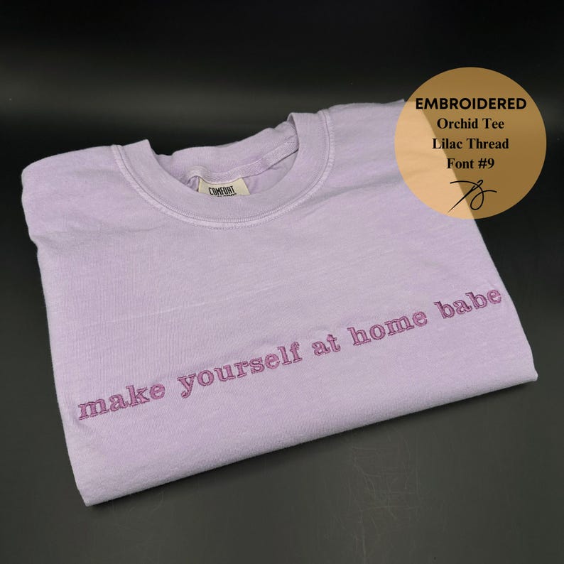 May include: A lavender colored t-shirt with the text "make yourself at home babe" embroidered in pink thread.