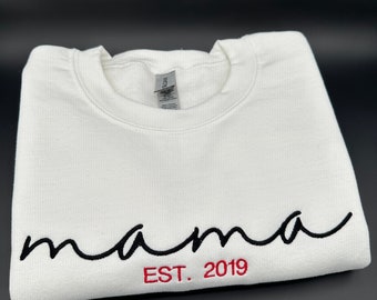 May include: White sweatshirt with black cursive text that says "mama" and red text that says "EST. 2019"
