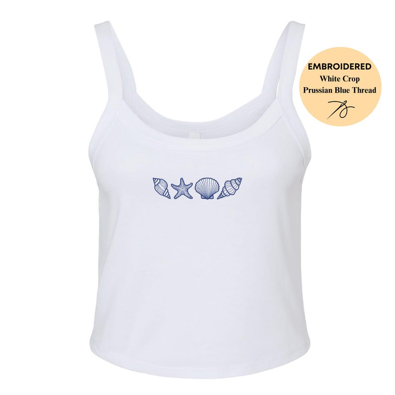 May include: White crop top with a scoop neck and thin straps. The top features an embroidered design of seashells and a starfish in Prussian blue thread. The image includes a circular graphic that reads "Embroidered White Crop Prussian Blue Thread".