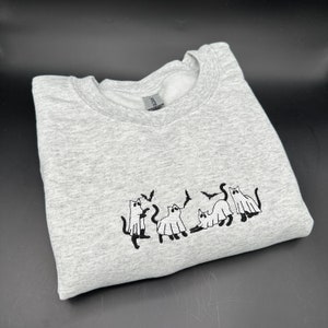 Peut inclure: Un sweat-shirt gris avec un motif brod&eacute; noir de cinq chats habill&eacute;s en fant&ocirc;mes. Les chats portent des costumes de fant&ocirc;mes avec des chauves-souris qui volent autour d'eux.