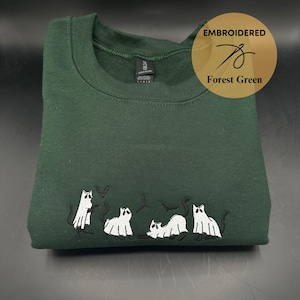 Peut inclure: Sweat-shirt vert for&ecirc;t avec des chats fant&ocirc;mes et des chauves-souris blancs brod&eacute;s. Le sweat-shirt a un col rond et est fait d'un tissu doux et confortable.