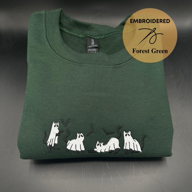 Peut inclure: Sweat-shirt vert for&ecirc;t avec des chats fant&ocirc;mes et des chauves-souris blancs brod&eacute;s. Le sweat-shirt a un col rond et est fait d'un tissu doux et confortable.