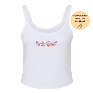 May include: White crop top with a scoop neck and thin straps. The top features an embroidered design of seashells in red thread. The text "EMBROIDERED White Crop Red Thread" is in a circle on the right.