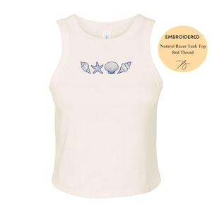 May include: Cream-colored racerback tank top with embroidered blue seashells and a starfish design. The tank top has a round neckline and is sleeveless. The text on the image says "Embroidered Natural Racer Tank Top Red Thread".
