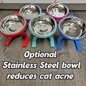 May include: A selection of elevated stainless steel pet bowls in red, purple, teal, pink, and blue. Each bowl is supported by a stand of the same colour. The image includes the text: "Optional Stainless Steel bowl reduces cat acne."