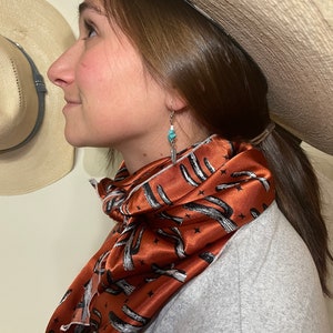 Peut inclure: Une femme portant un foulard en soie à motifs marron et blanc avec un chapeau de cow-boy. Le foulard a un motif de cactus.