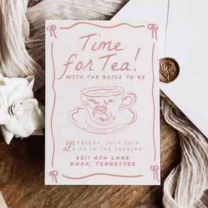 Pode incluir: Um convite rosa claro com o texto "Time for Tea!" e uma ilustração de xícara de chá. Um envelope branco com um selo de cera dourada e uma fita decorativa também estão presentes. O convite inclui a data, hora e local.