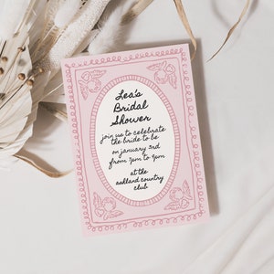 Pode incluir: Um convite rosa para um ch&aacute; de panela com uma borda decorativa e o texto "Lea's Bridal Shower" em fonte cursiva preta. O convite detalha a data, hora e local do evento.